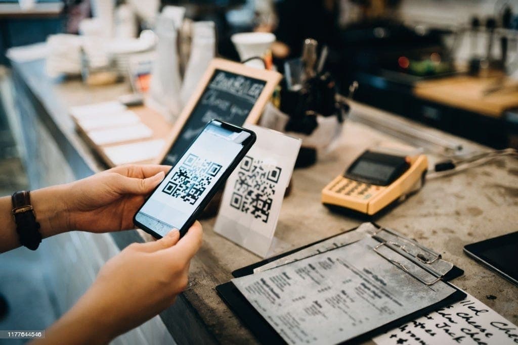 Gast scannt am Tresen einen QR-Code mit dem Smartphone